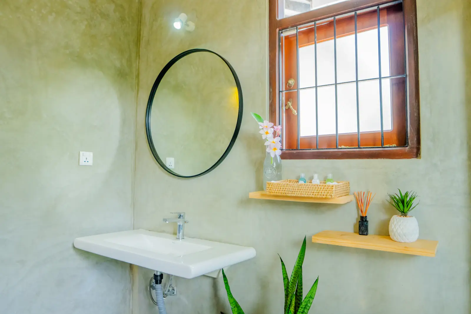 Salle de bains lumineuse avec lavabo, miroir rond et fenêtre en bois